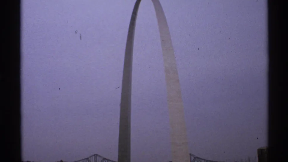 1972 Saint Louis frame with the Gateway Arch centered against a muted cloudy sky, with faint bridge detail and visible film edge at the sides.