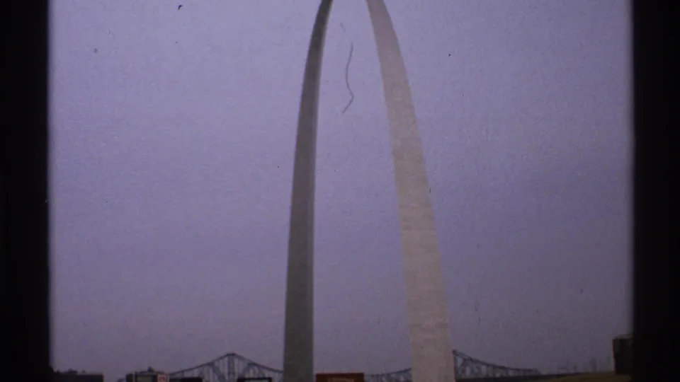 1972 Saint Louis 8mm frame showing the Gateway Arch extending upward from the riverfront area, with a bridge and dark building shapes near the bottom.
