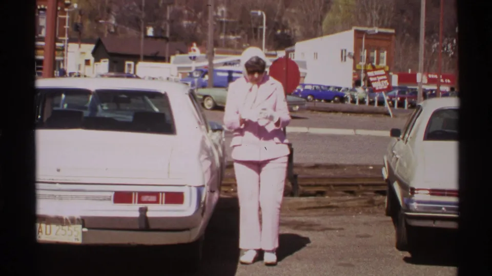 The woman stands near the white car in a Saint Louis parking lot, appearing to examine a tire gauge in bright daylight.