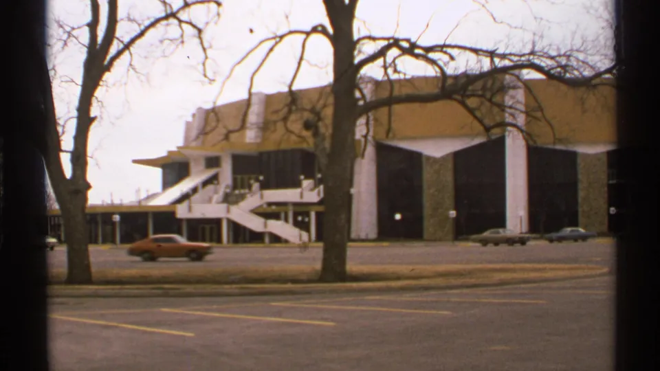 1972 Tulsa home-movie frame of the Mabee Center exterior, with early-1970s cars moving past the parking lot.