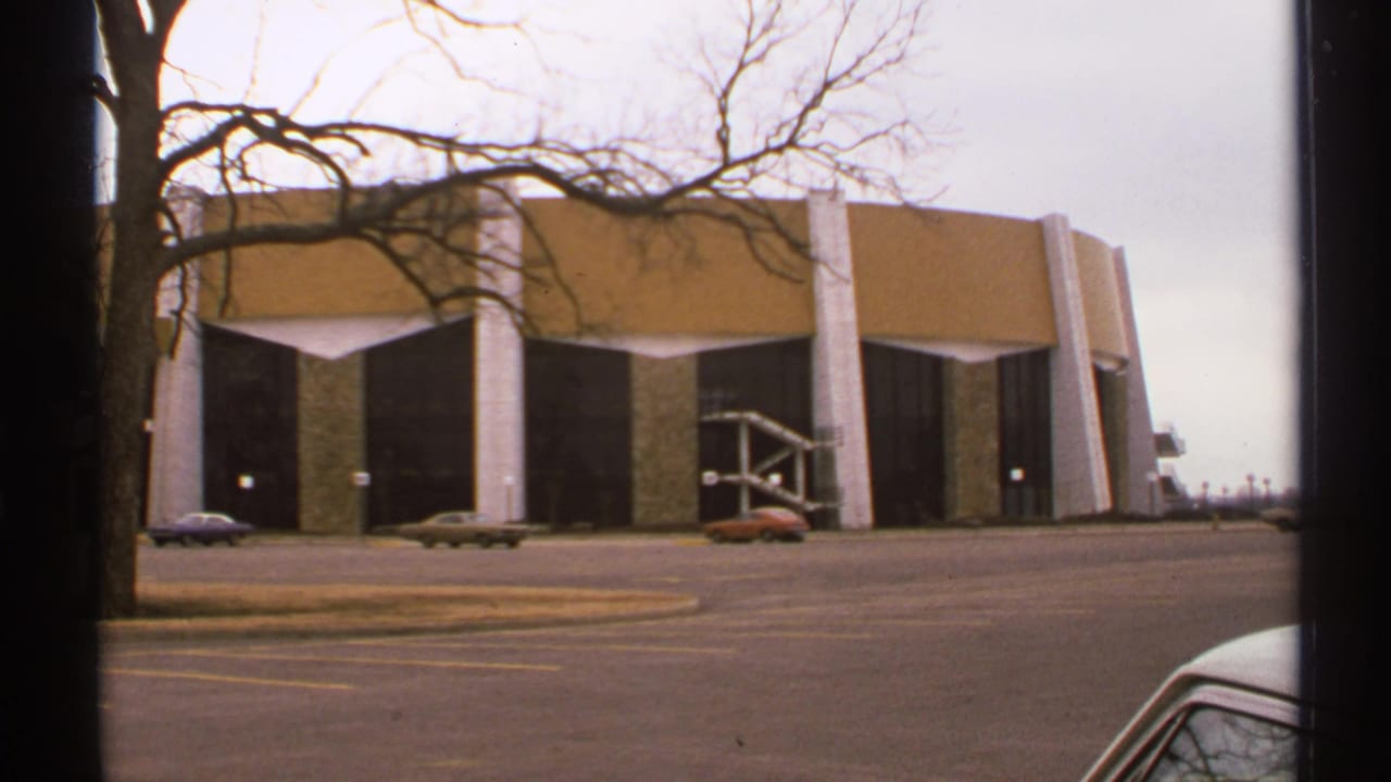 Modernist building across a parking lot with bare trees and vintage cars.