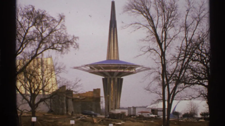 1972 Tulsa frame showing a spired tower with a wide circular platform, bare winter trees, low buildings, cars, and construction debris nearby.
