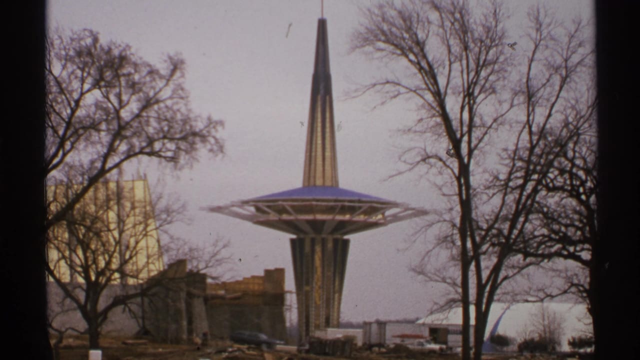 1972 Tulsa home-movie frame showing the Oral Roberts University Prayer Tower rising behind bare trees and unfinished campus ground.
