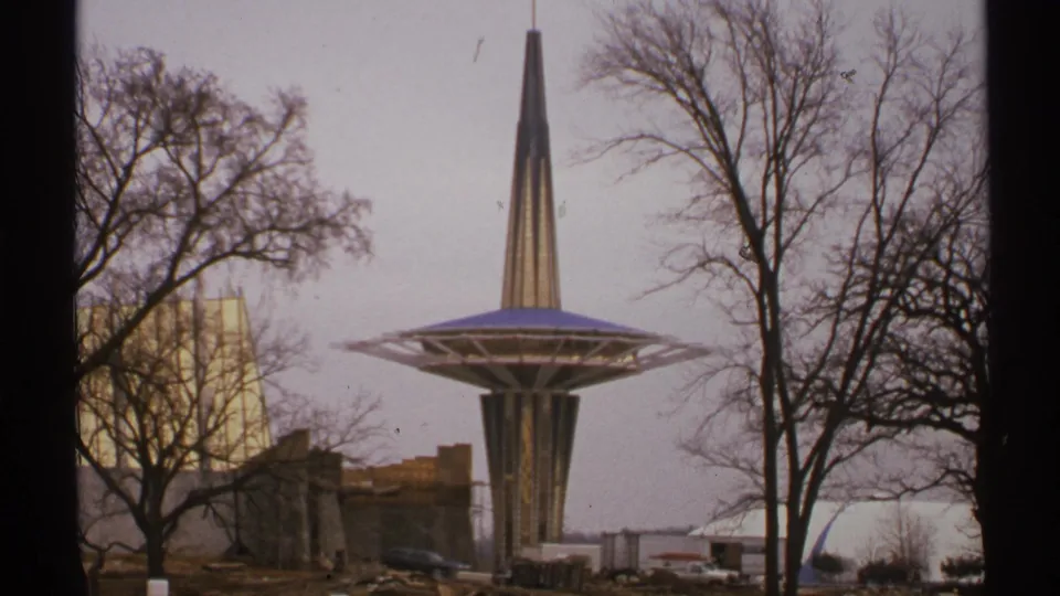 1972 Tulsa home-movie frame showing the Oral Roberts University Prayer Tower rising behind bare trees and unfinished campus ground.