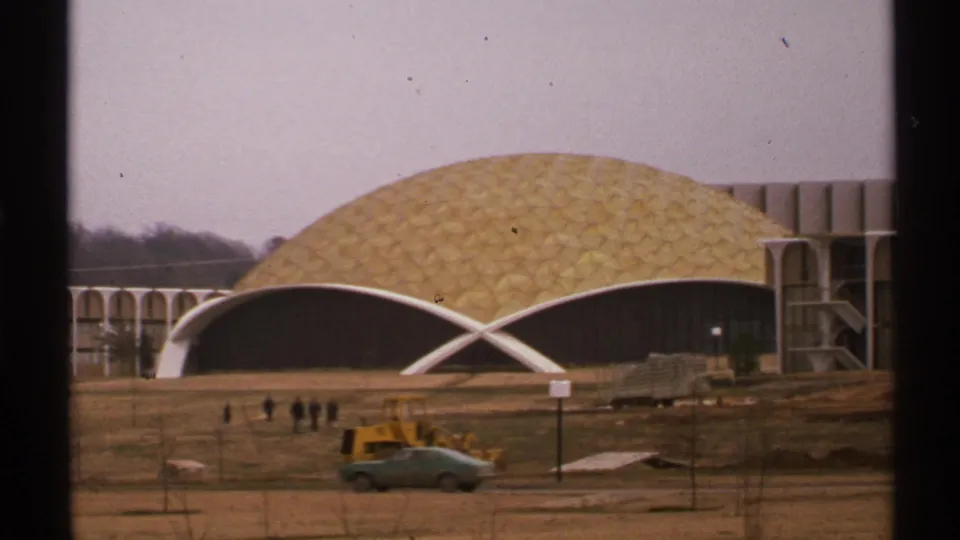 1972 Tulsa frame of Howard Auditorium's golden dome and white arch facade, with workers, bulldozer, and parked green car on the grounds.