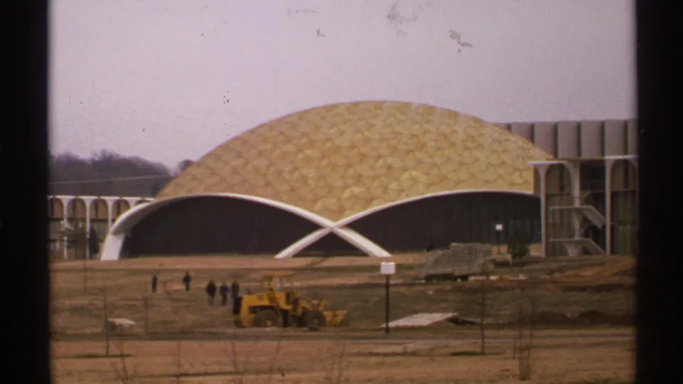 1972 Tulsa 8mm frame showing a gold geodesic dome building under construction with white arches, bare grounds, pedestrians, and a yellow loader.