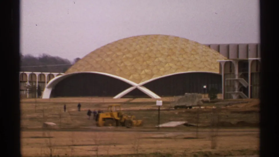 1972 Tulsa home-movie view of the geodesic dome building and white arched facade, with pedestrians and a loader on unfinished grounds.
