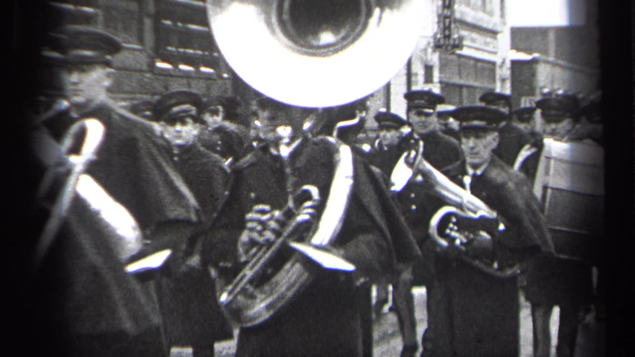 1937 Cleveland street parade footage shows uniformed band members in caps and capes playing brass instruments near storefronts.