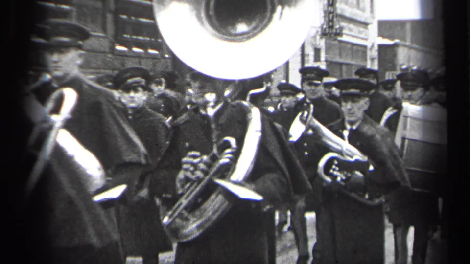 1937 Cleveland street parade footage shows uniformed band members in caps and capes playing brass instruments near storefronts.