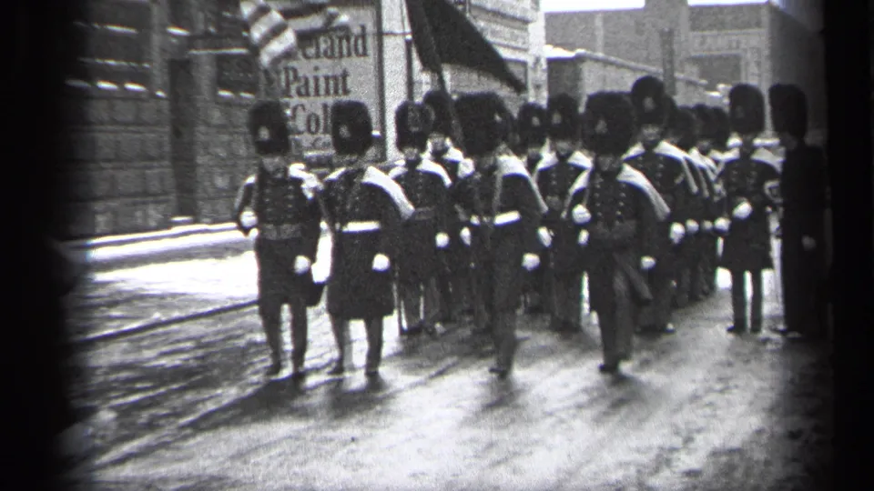 Wider 1937 Cleveland view of band members in formation marching along wet pavement past storefront signage.