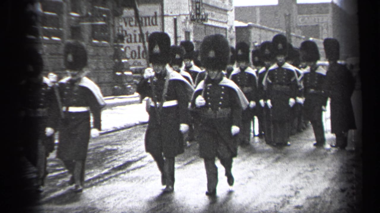 Rows of uniformed marchers continue down the street with storefront signs behind them.