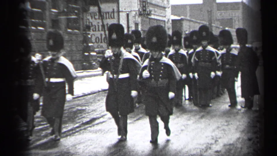 Uniformed parade participants march in formation through Cleveland, with a Cleveland Paint Color sign visible behind them.