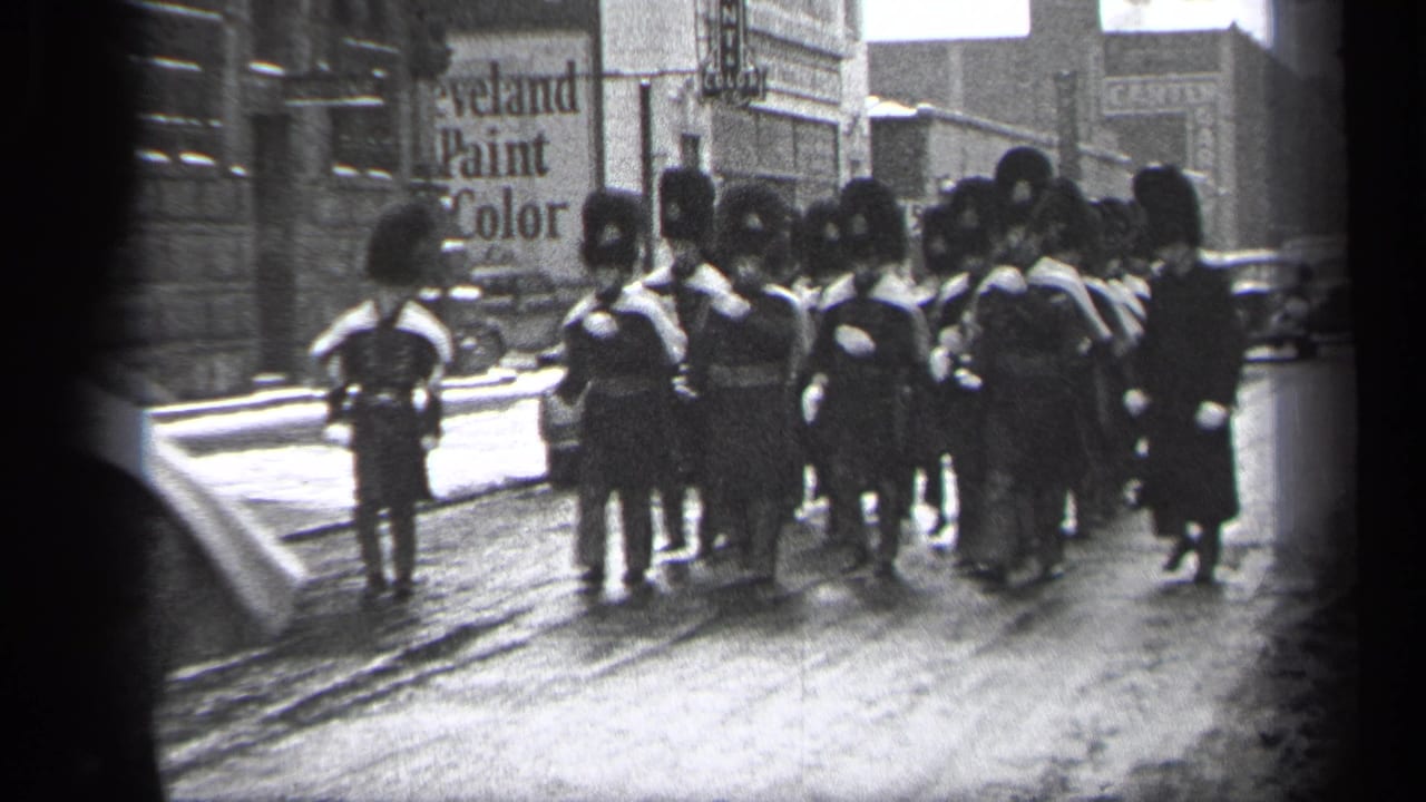 Uniformed marchers in tall dark hats approach on a Cleveland street.