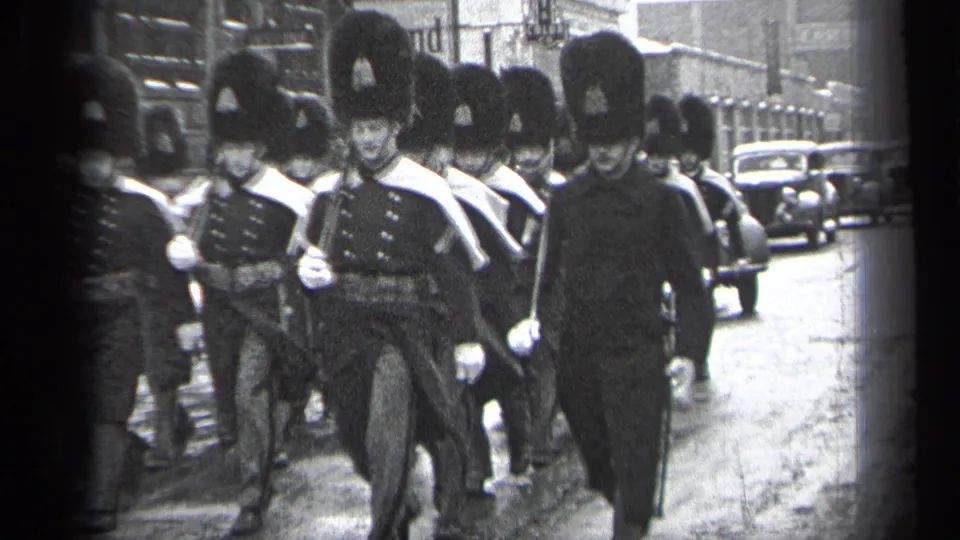 1937 Cleveland home-movie frame showing the parade group close to camera, with tall hats, dark uniforms, and street traffic behind.