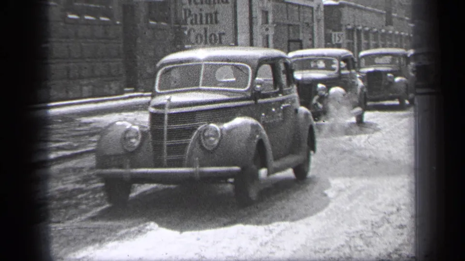 Cleveland 1937 street view with classic automobiles, wet-looking pavement, tall buildings, and painted storefront signage.