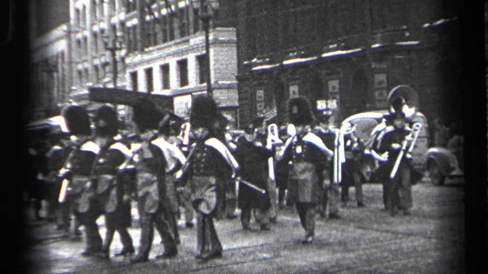 From behind the procession, uniformed band members move away along the Cleveland street with brass instruments and parked cars in view.