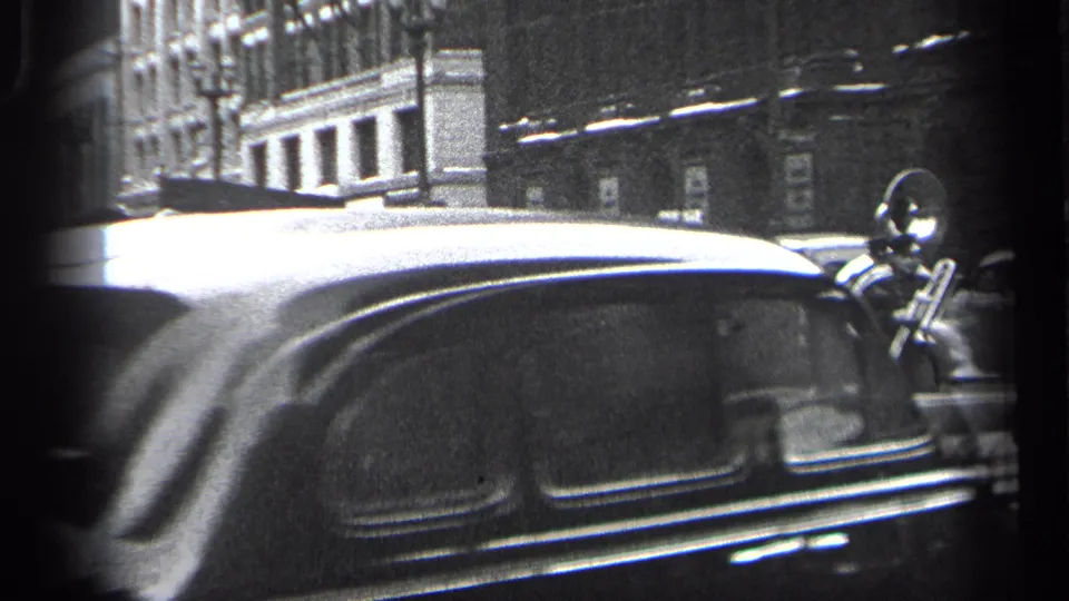 A passing automobile briefly obscures the 1937 Cleveland marching band, leaving a brass player visible at the right edge.