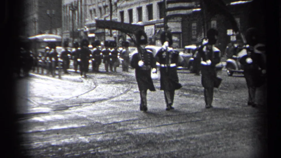 Three uniformed participants walk away through a Cleveland street scene in 1937, with classic automobiles and bystanders lining the route.