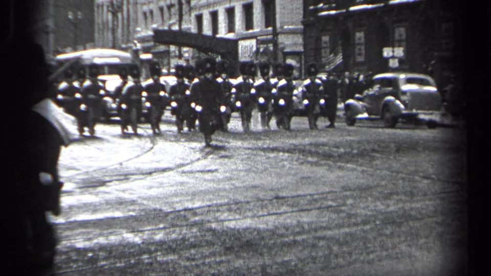 The procession continues down a Cleveland street, with a larger formation of uniformed marchers, spectators, streetcar tracks, and 1930s automobiles visible.