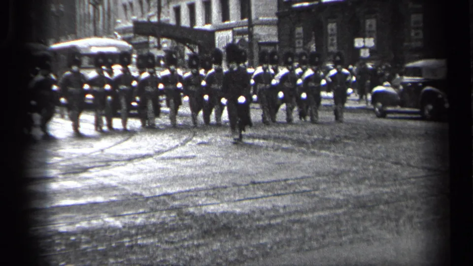 1937 Cleveland street frame with a small pedestrian crossing ahead of a uniformed marching formation on wet pavement.