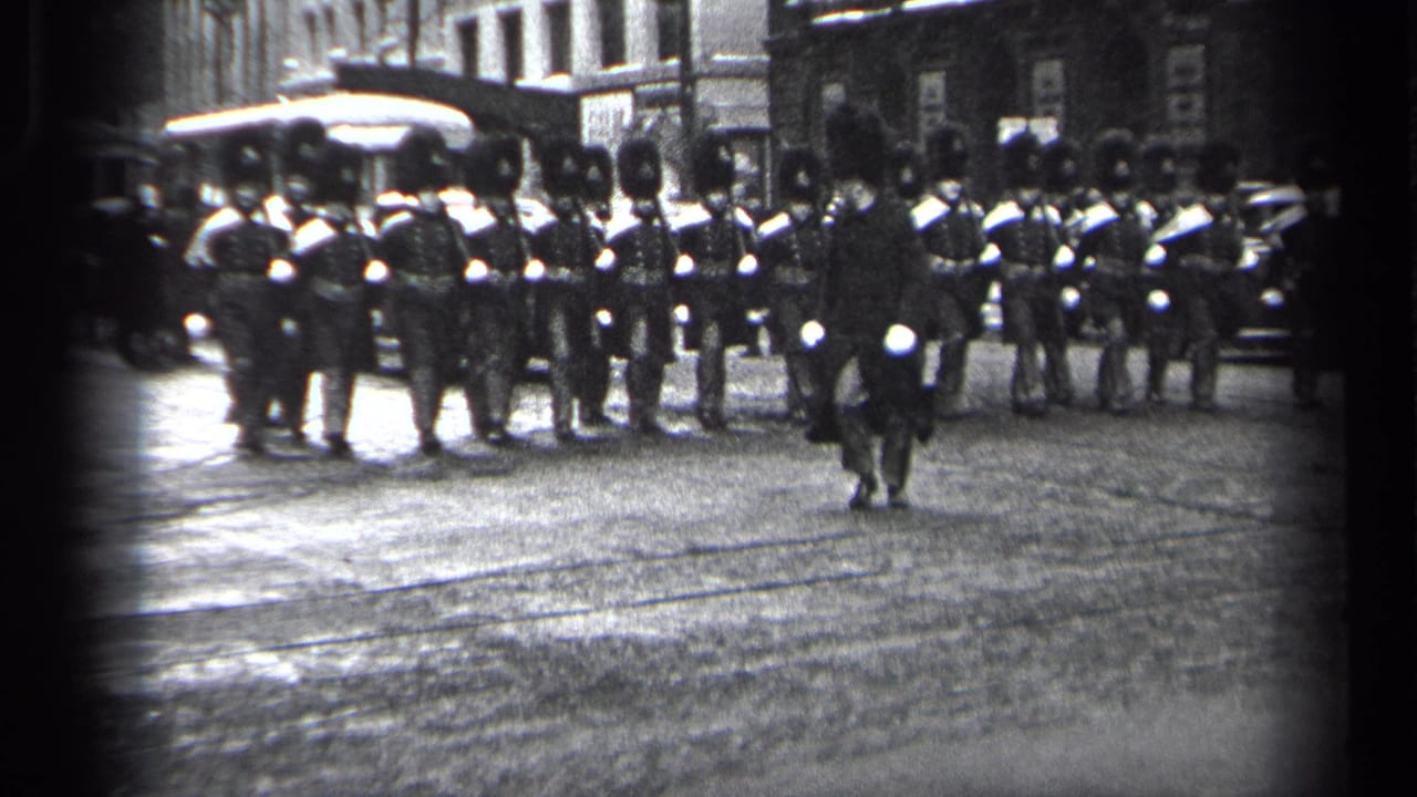 1937 Cleveland 8mm frame showing uniformed marchers in tall hats forming across an urban street with buildings and vehicles behind them.