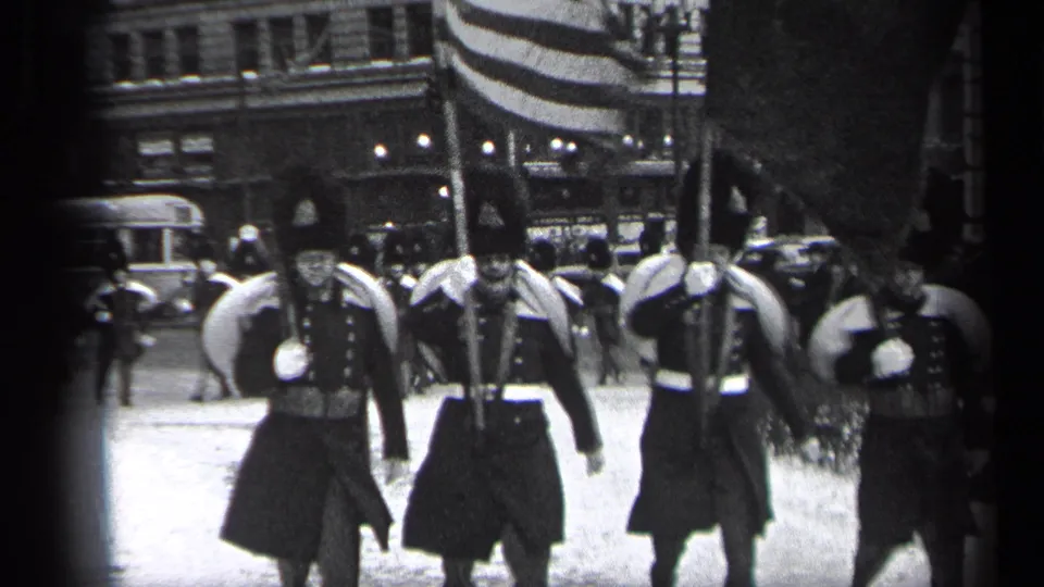 A closer 1937 Cleveland parade view shows uniformed marchers in tall hats passing the camera with flags and rifles.