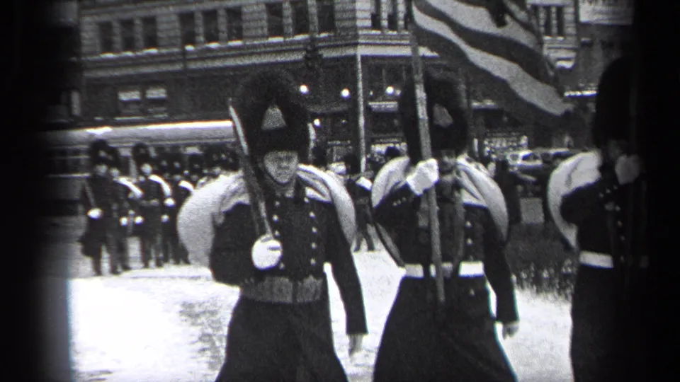 Near the end of the Cleveland parade clip, uniformed marchers pass close by as a large flag crosses the frame.