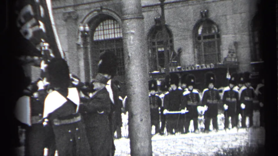 1937 Cleveland home-movie frame showing soldiers in dark uniforms and tall hats lined up outside a stone building during a public ceremony.