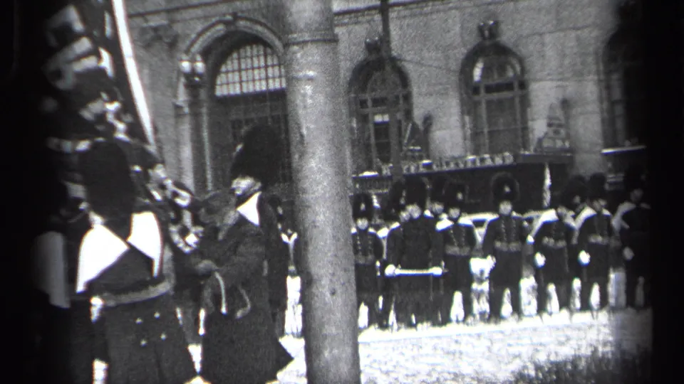 Uniformed personnel stand at attention outside a grand stone building in Cleveland, with home-movie framing partly obscured by nearby viewers.