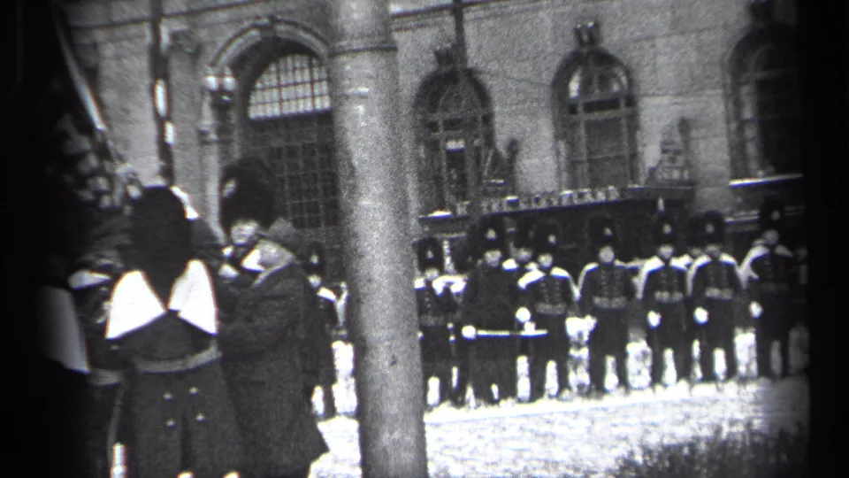 1937 Cleveland home-movie frame showing guards in tall ceremonial hats near a stone facade, partially obscured by a tree trunk.
