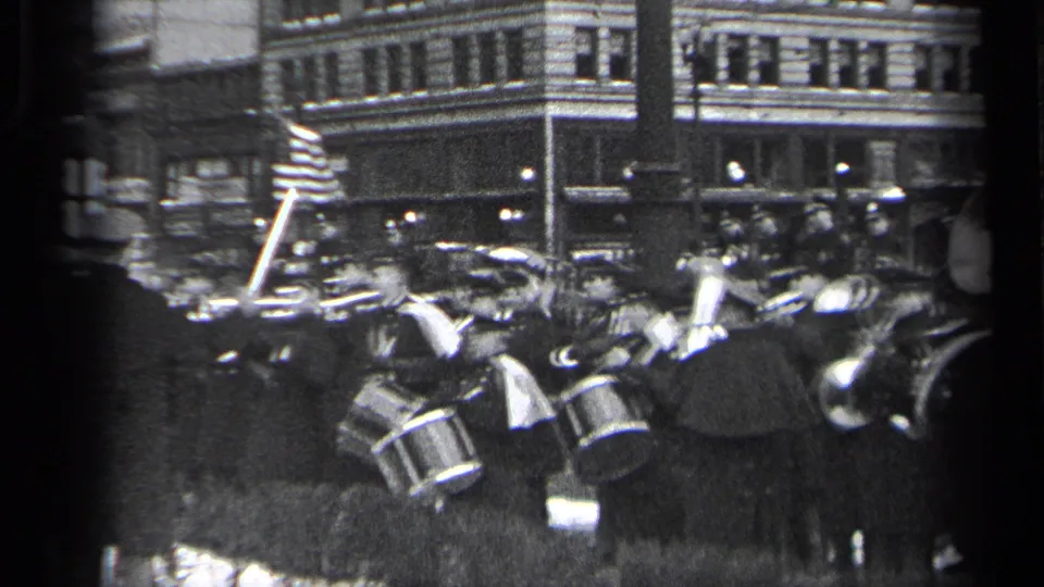 1937 Cleveland frame showing a marching band with drums, flags, and uniformed participants during an outdoor ceremony.