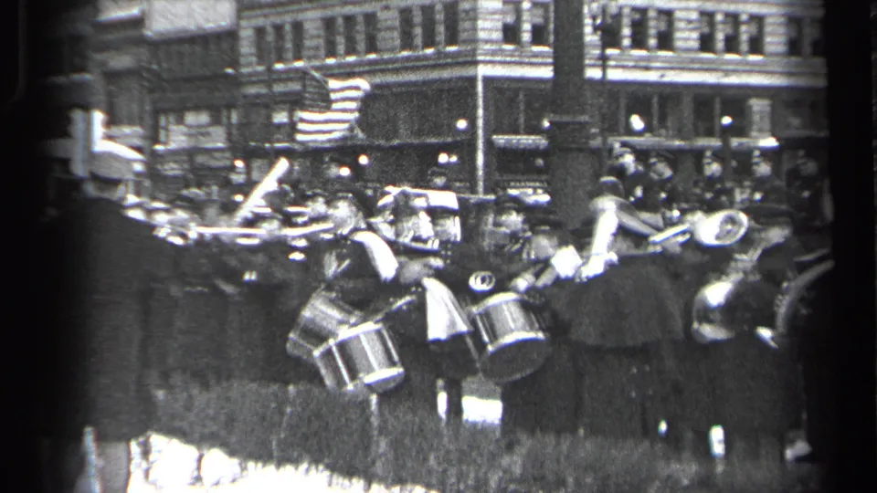 Uniformed musicians in a 1937 Cleveland parade play drums and brass instruments as spectators gather near tall street-side buildings.