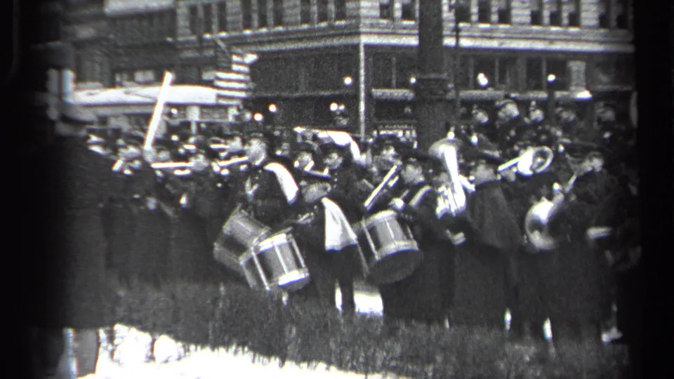 1937 Cleveland parade frame showing uniformed band members, drums, brass instruments, spectators, and an American flag in a busy street setting.