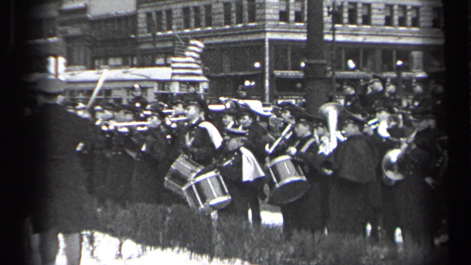 1937 Cleveland street scene with a marching band performing beside spectators and downtown buildings.