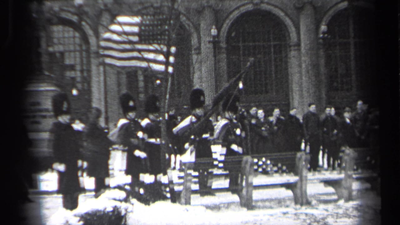 Ceremonial guards stand near a raised American flag with spectators in front of arched windows.