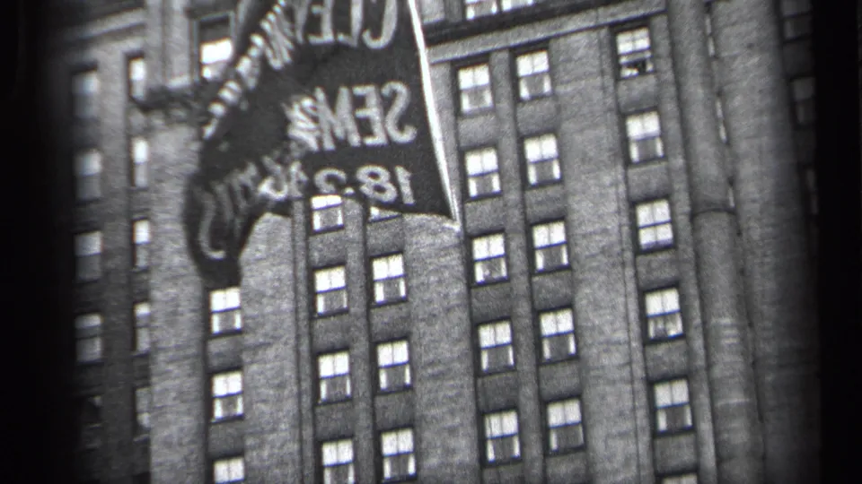1937 Cleveland home-movie frame showing a raised flag with reversed text against a tall masonry building.