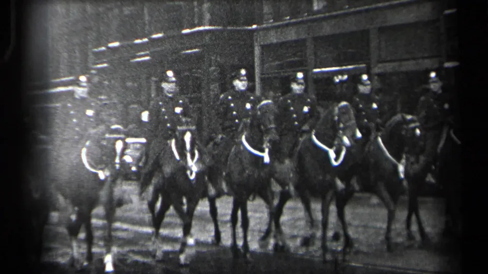 Mounted police officers and horses move in a line on a Cleveland street, with storefront-like buildings behind them.