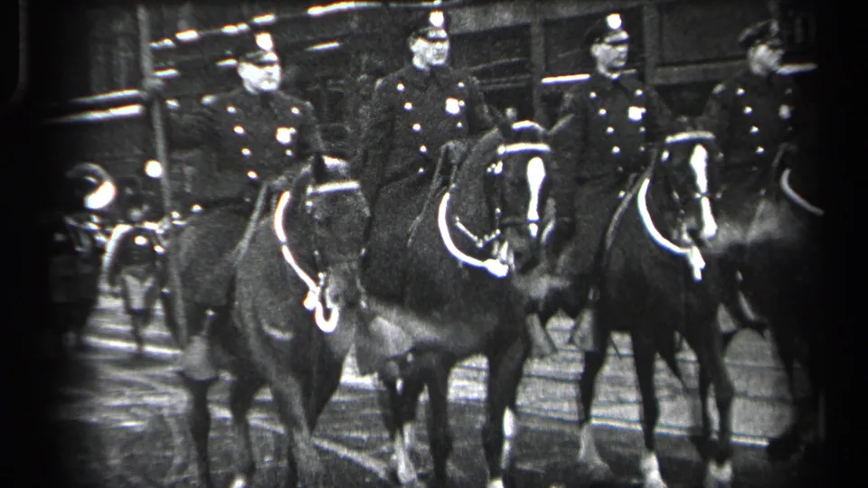 Mounted police in Cleveland ride past the camera while a pedestrian stands near the street edge in the foreground.