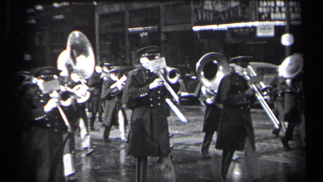 Uniformed marching band members play brass instruments on a wet city street at night.