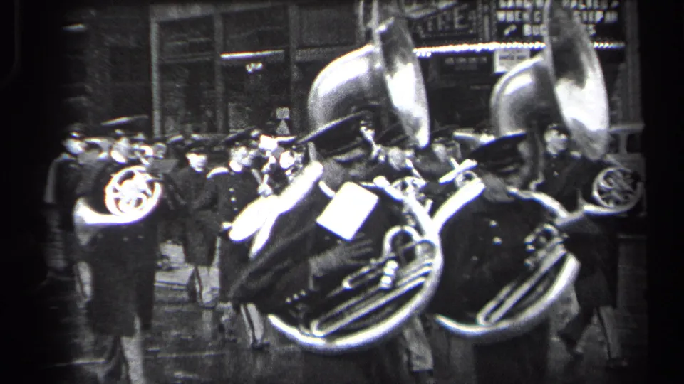 Nighttime 1937 Cleveland home-movie frame showing horn players and nearby spectators on a wet urban street.