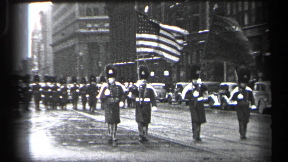 1937 Cleveland parade frame with uniformed marchers advancing along a wet street beneath a large American flag.