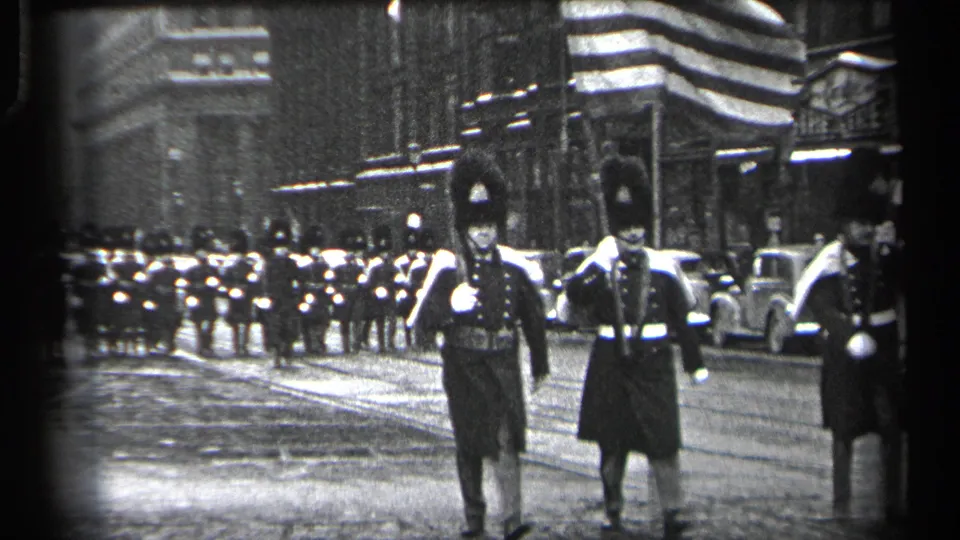 In 1937 Cleveland footage, ceremonial uniformed marchers approach along a downtown street with a larger formation behind them.