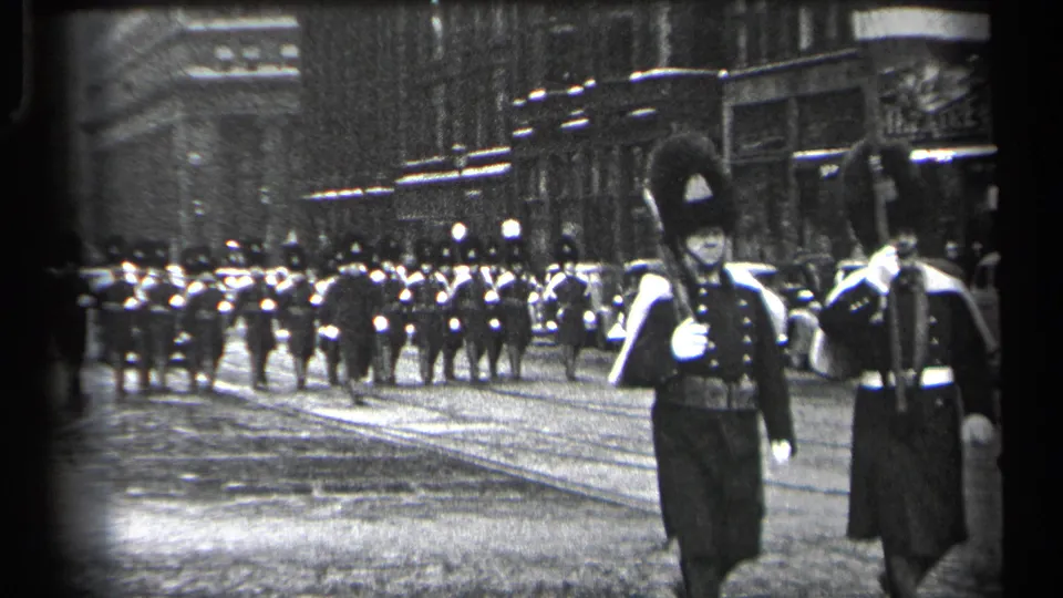 Two ceremonial marchers in tall dark hats move past the camera as the Cleveland street formation continues in the background.