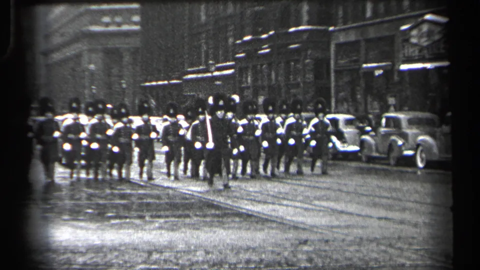 The Cleveland parade formation continues through the urban street, with ceremonial uniforms, parked cars, and storefront facades visible.