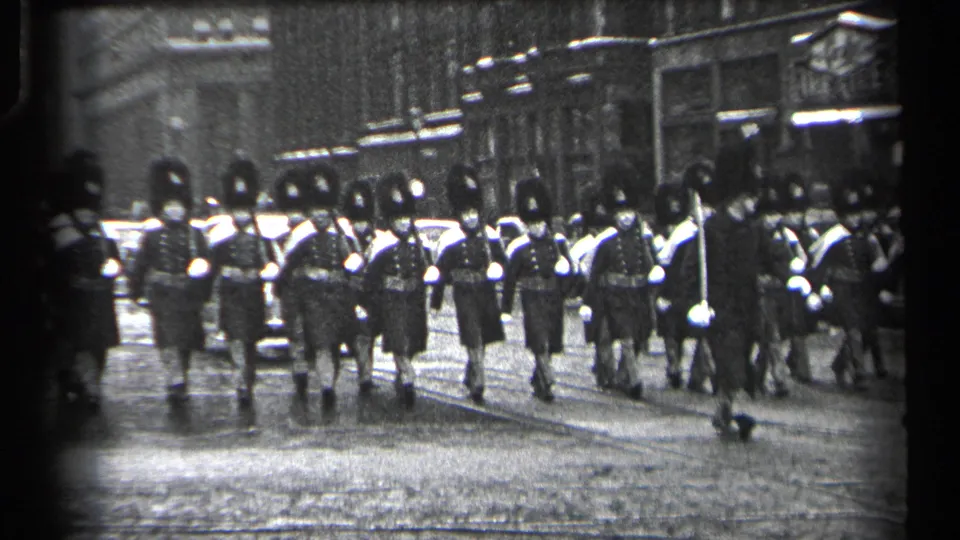 The Cleveland parade group passes nearer to the camera, showing dark uniforms, tall hats, and reflective wet pavement.