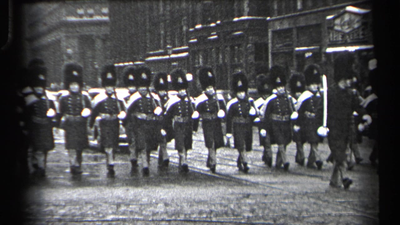In 1937 Cleveland, uniformed British Guards appear to march toward the camera along a cobblestone city street.