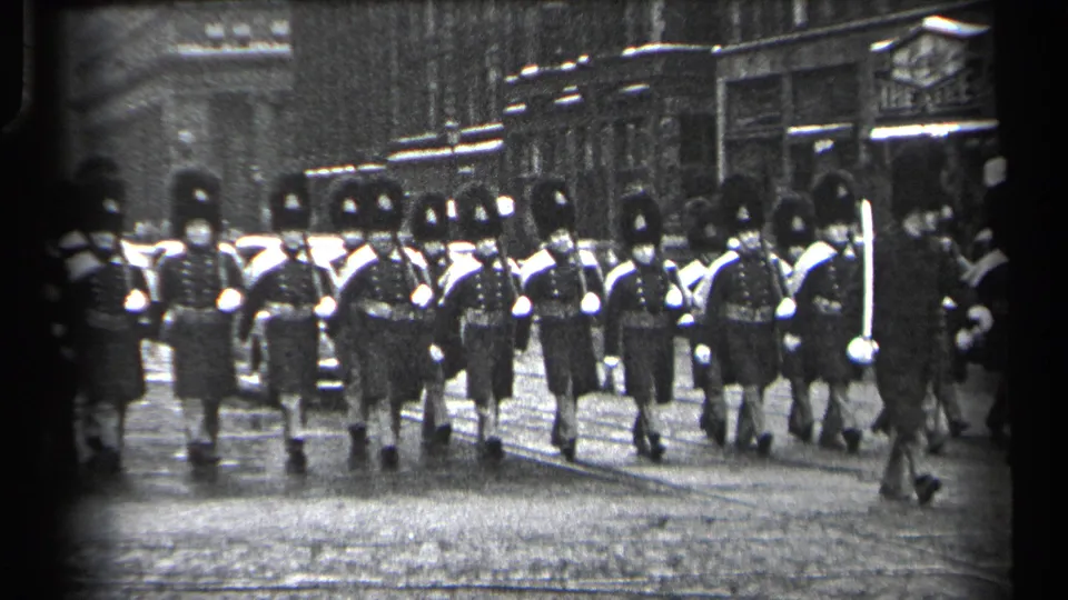 In 1937 Cleveland, uniformed British Guards appear to march toward the camera along a cobblestone city street.