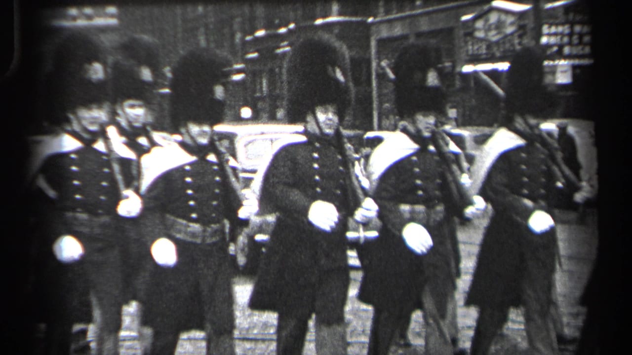 Ceremonial guards in tall hats march in formation on a city street.