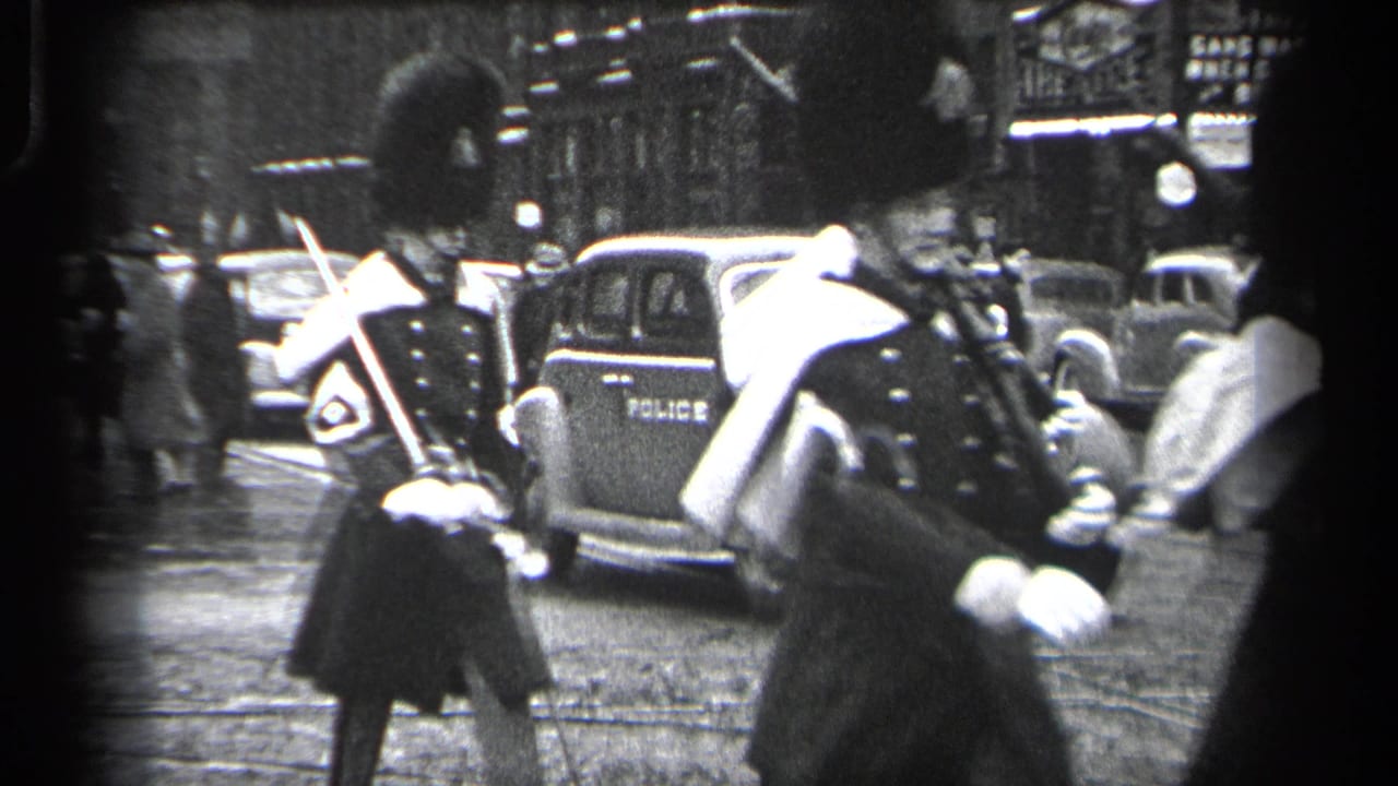 Uniformed guards with rifles pass a police-marked car on a city street.