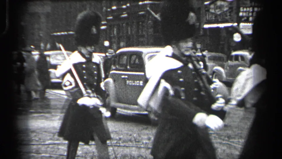 Ceremonial guards in 1937 Cleveland move past a police-marked vehicle and period cars during a street procession.